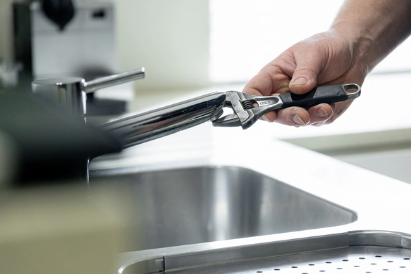Plumber using adjustable wrench on kitchen tap fixture for emergency burst pipe repair in Perth.
